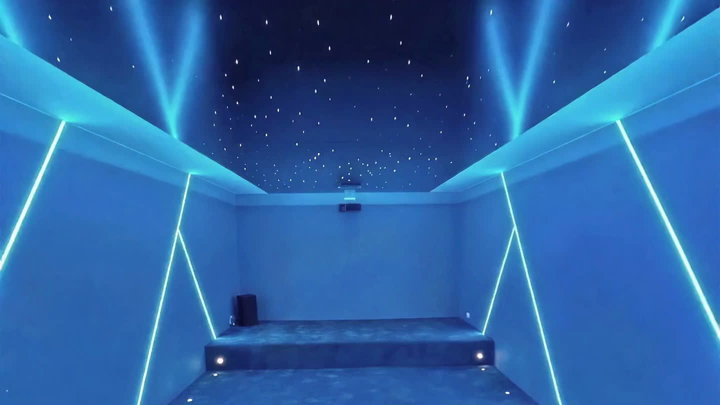 Fibre-optic starfield across a home cinema ceiling above cyan LED lines and tiered seating