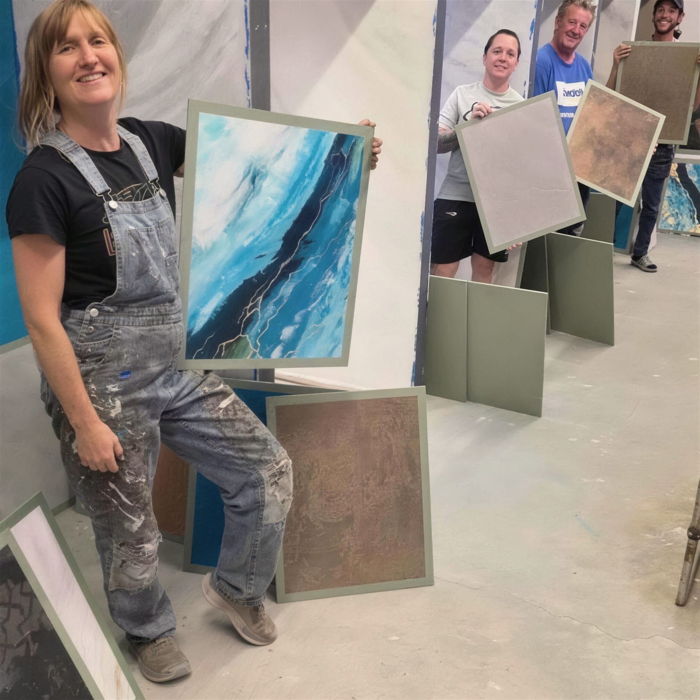 A smiling trainee in plaster-flecked dungarees holds up her finished teal sample board while classmates behind present theirs.