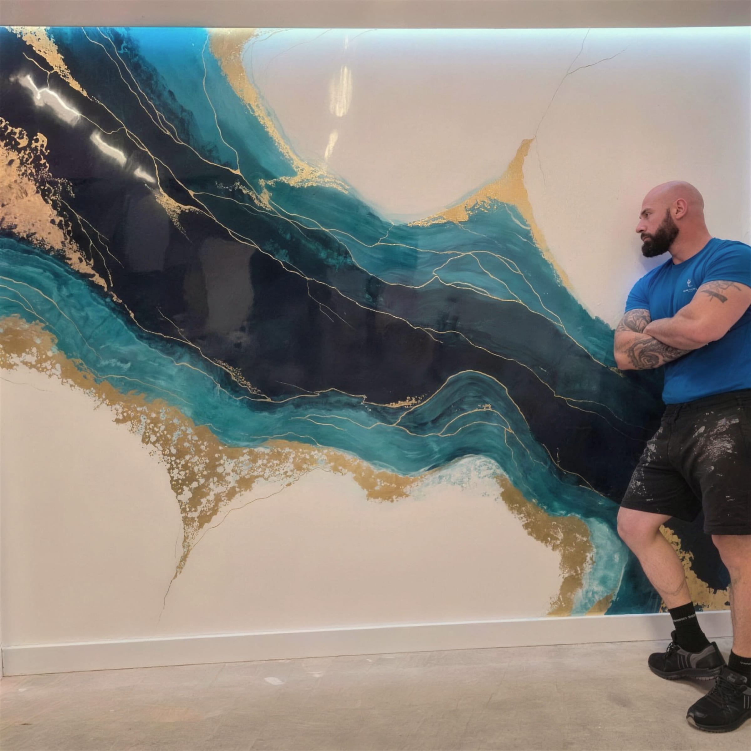 Darren leans, arms crossed, against a wall-sized teal, navy and gold decorative finish sweeping diagonally across a white ground.