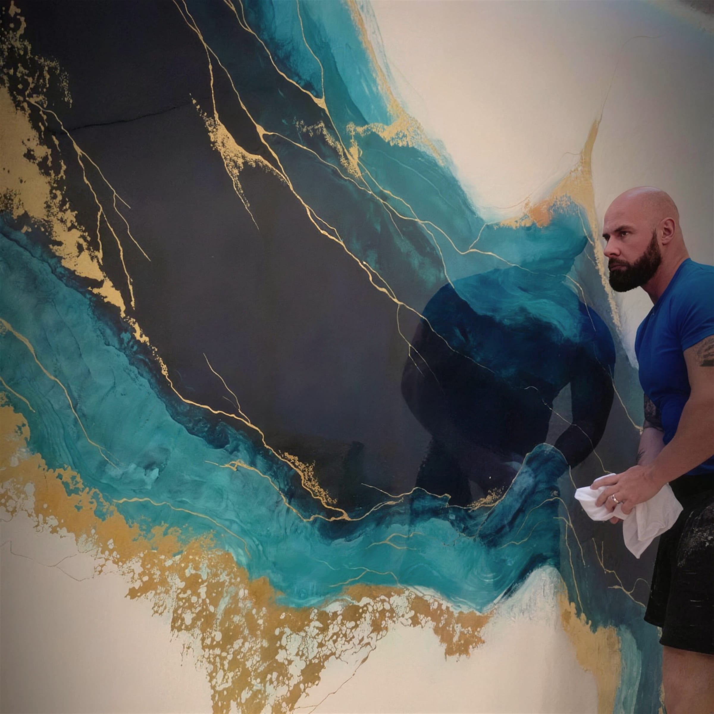 Darren, cloth in hand, works over the teal and gold feature wall at close range, the layered finish filling the frame around him.
