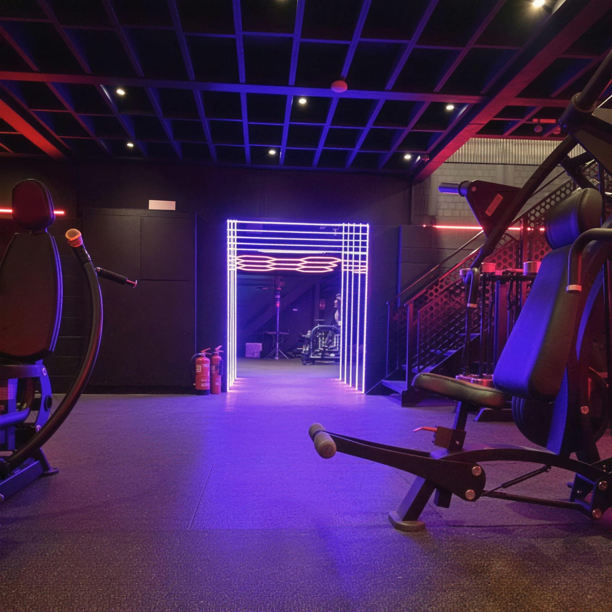 Dark gym interior with black grid ceiling and a glowing blue-and-red LED portal framed at the end of the room.
