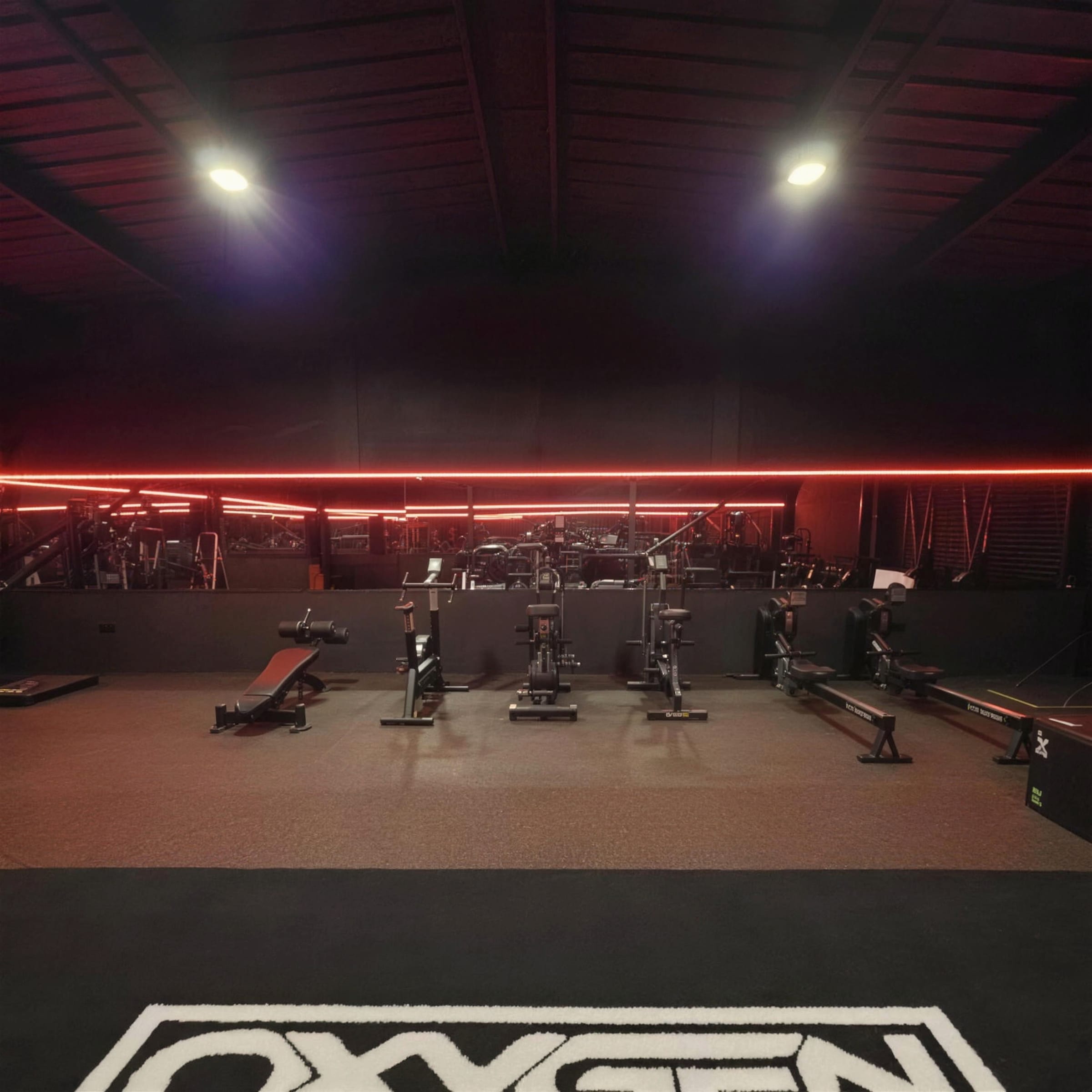 Symmetrical wide view of the dark gym with a continuous red LED line and the club logo on the floor.