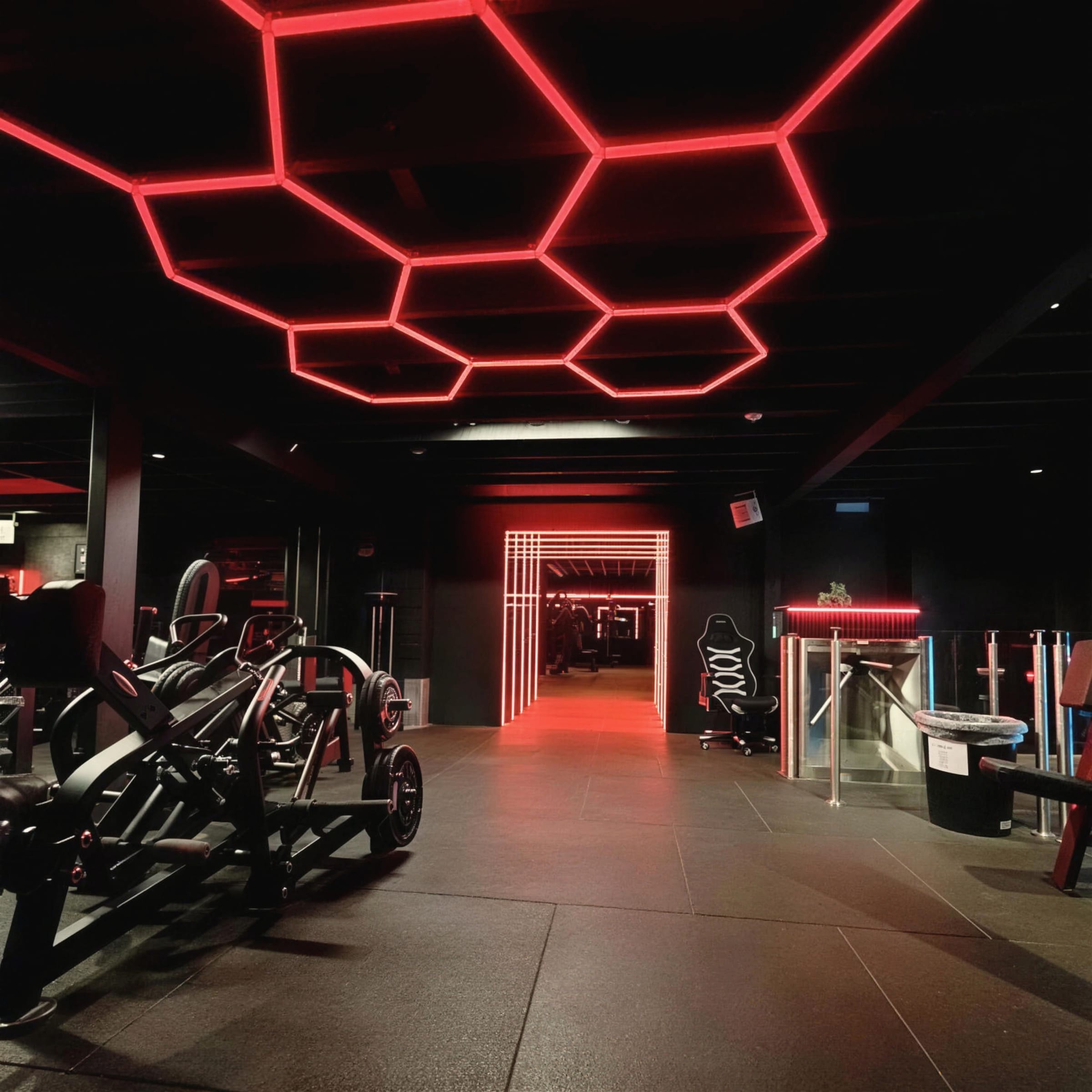 Red hexagonal LED canopy over the gym floor with a lit tunnel receding in the distance.
