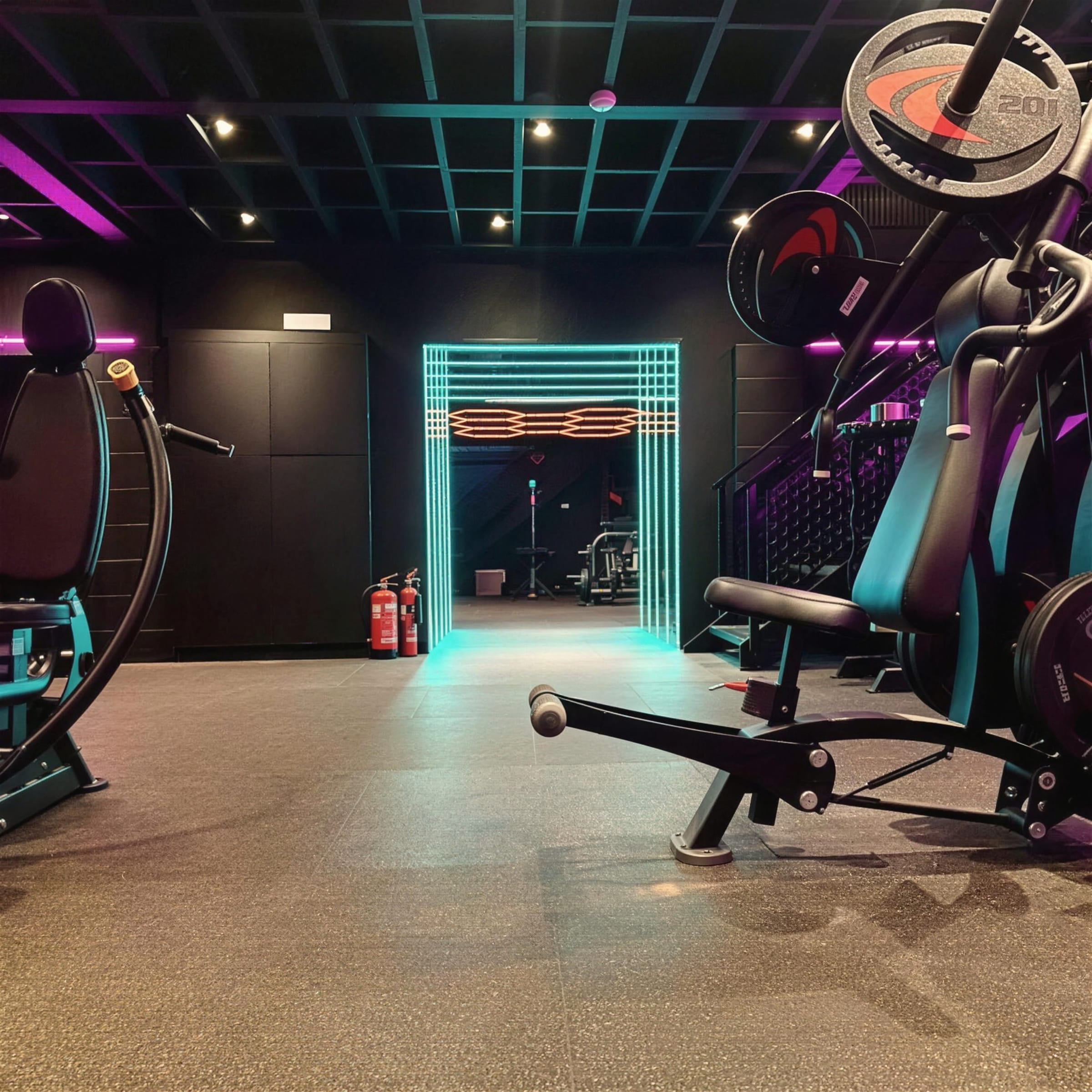 Teal LED portal glowing at the end of a dark gym corridor, machines framing either side.