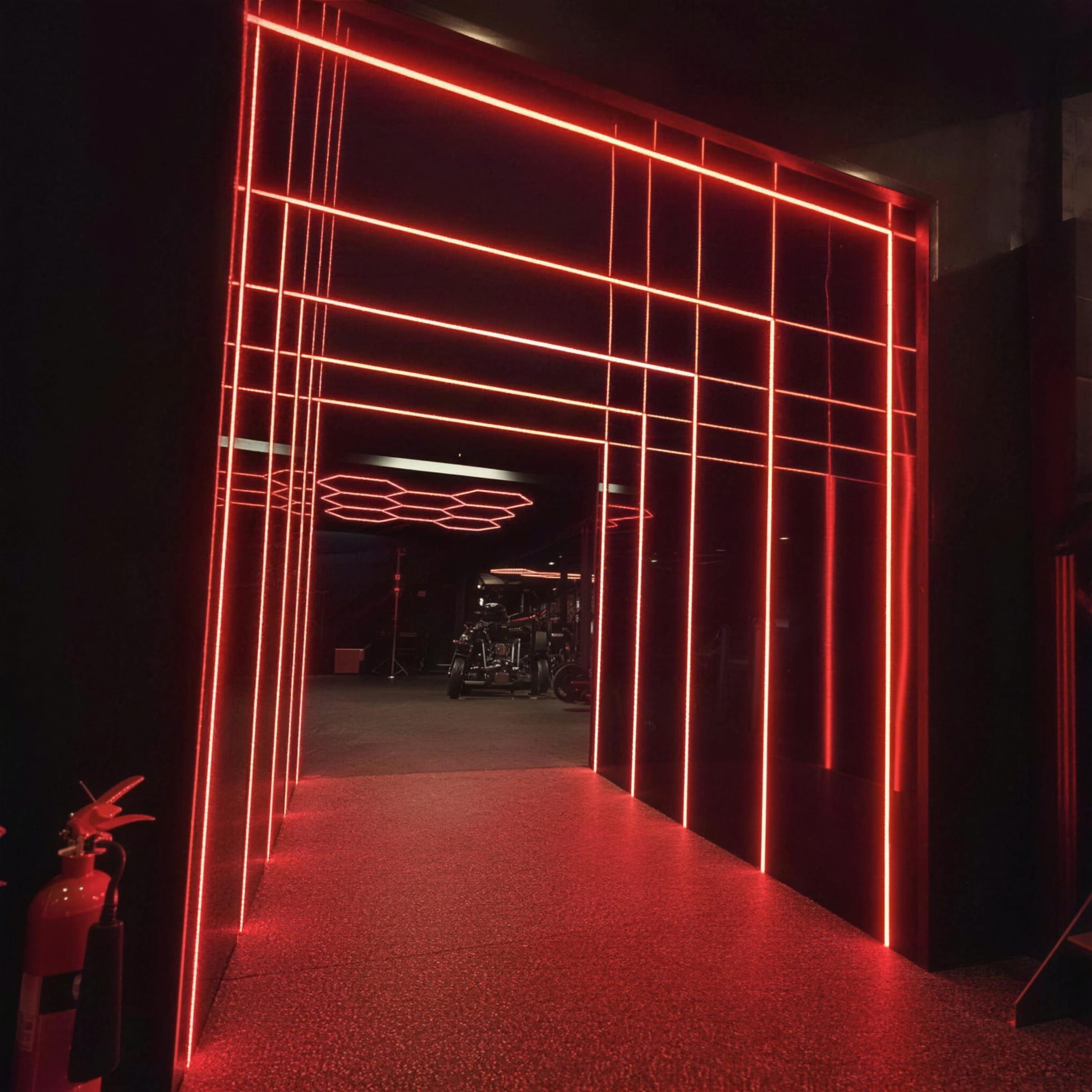 Red linear LED portal frames forming a glowing tunnel entrance into a dark gym, speckled floor washed in red light.