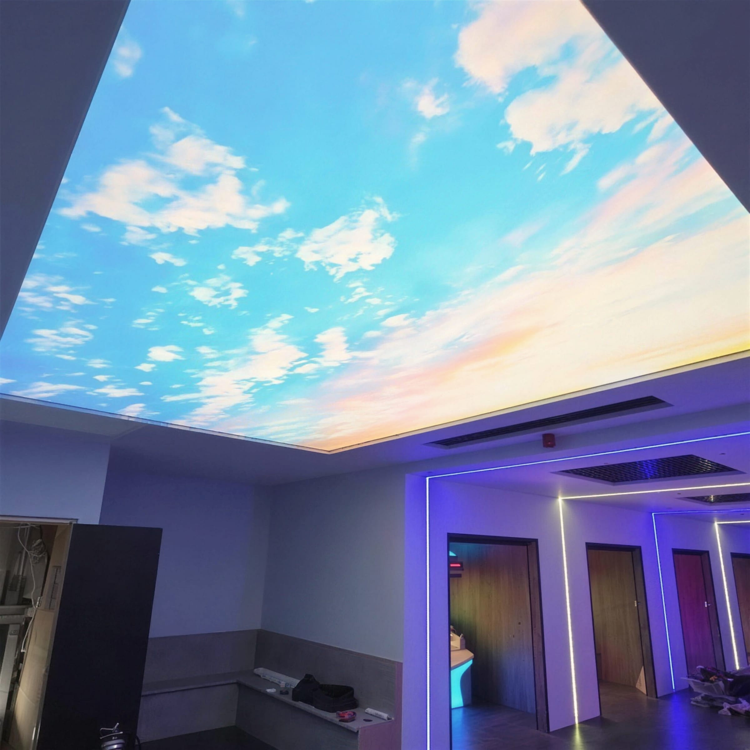 Illuminated printed sky stretch ceiling glowing above a salon corridor edged with neon-blue LED strips around changing room doorways.