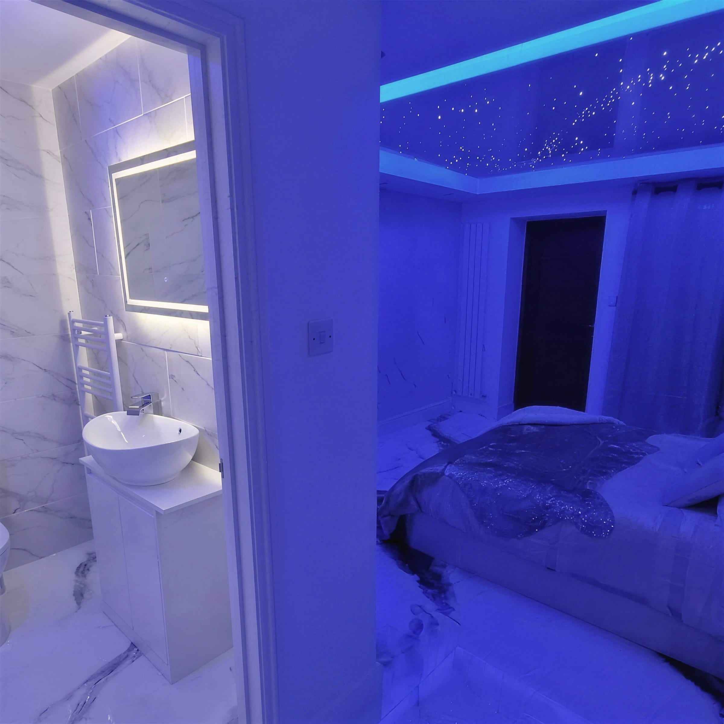 Bedroom at night with a fibre-optic star ceiling glowing above the bed, the ensuite beyond bathed in deep blue light.