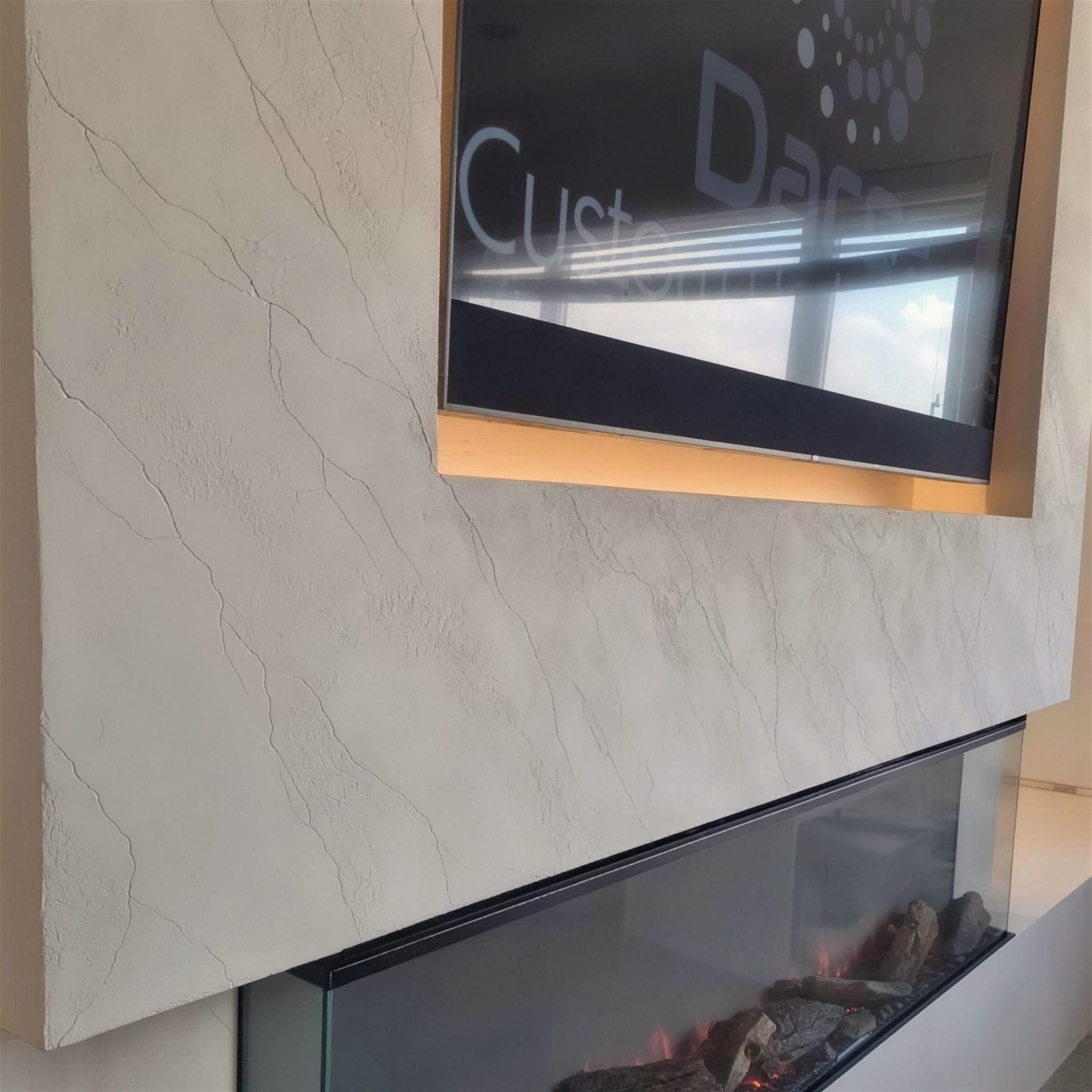 Angled detail of a cream travertine-effect plaster media wall wrapping a recessed TV above a lit log-effect electric fire.