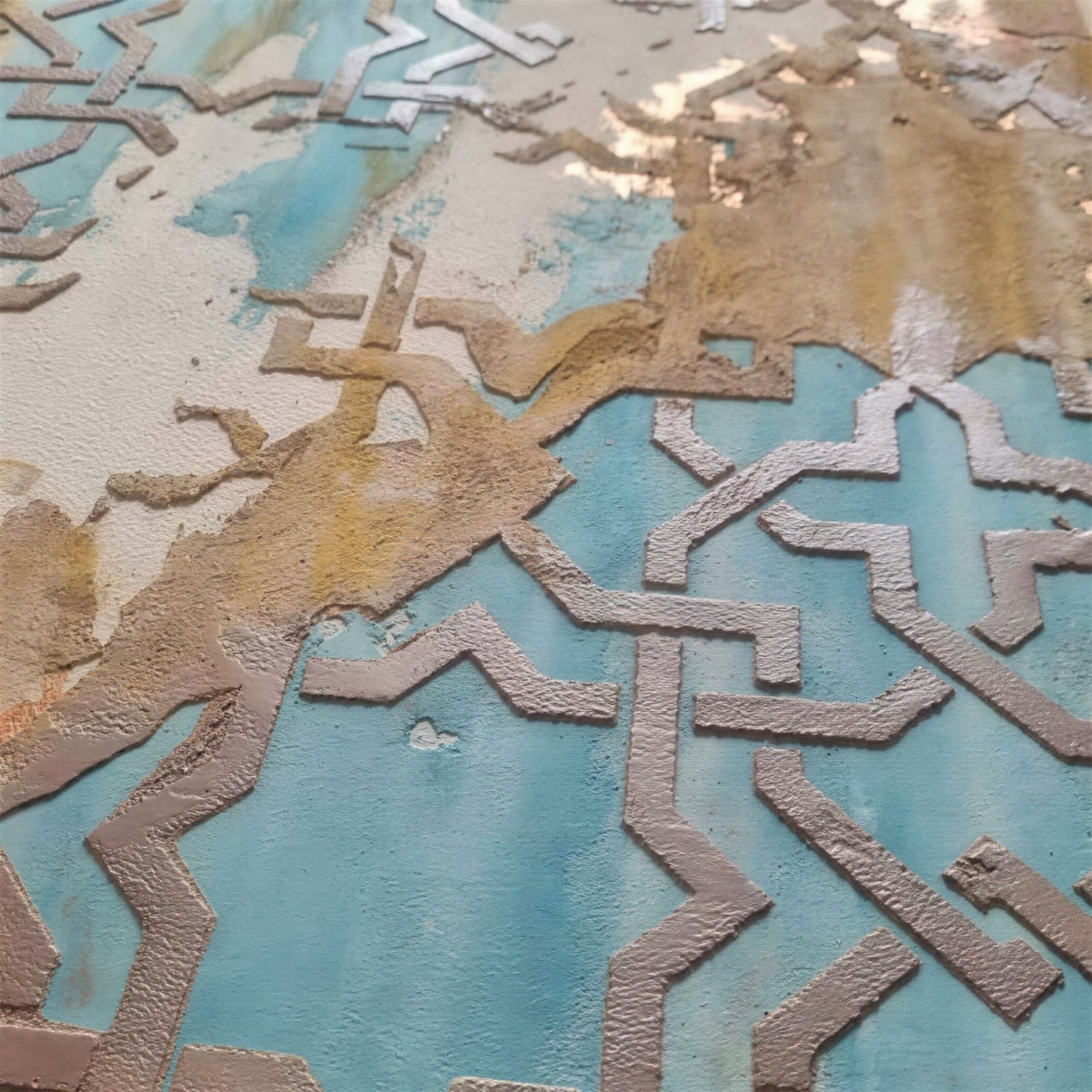 Macro of a distressed turquoise plaster surface with raised bronze geometric star-lattice stencilling and ochre patina.