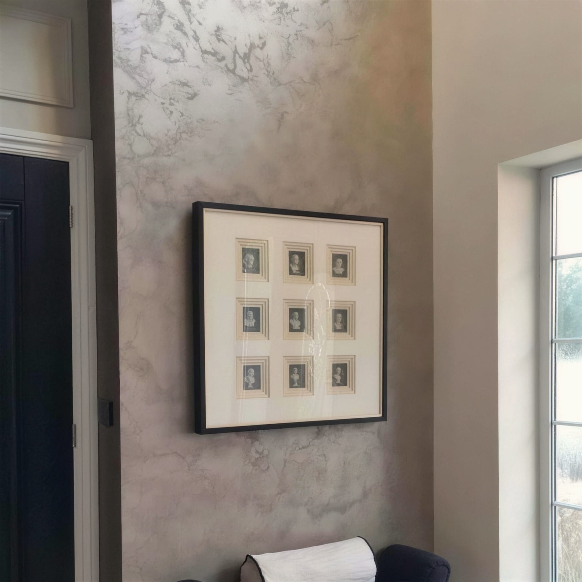 Silver-taupe metallic marbled plaster wall in a hallway, hung with a grid of framed miniature portraits beside a window.