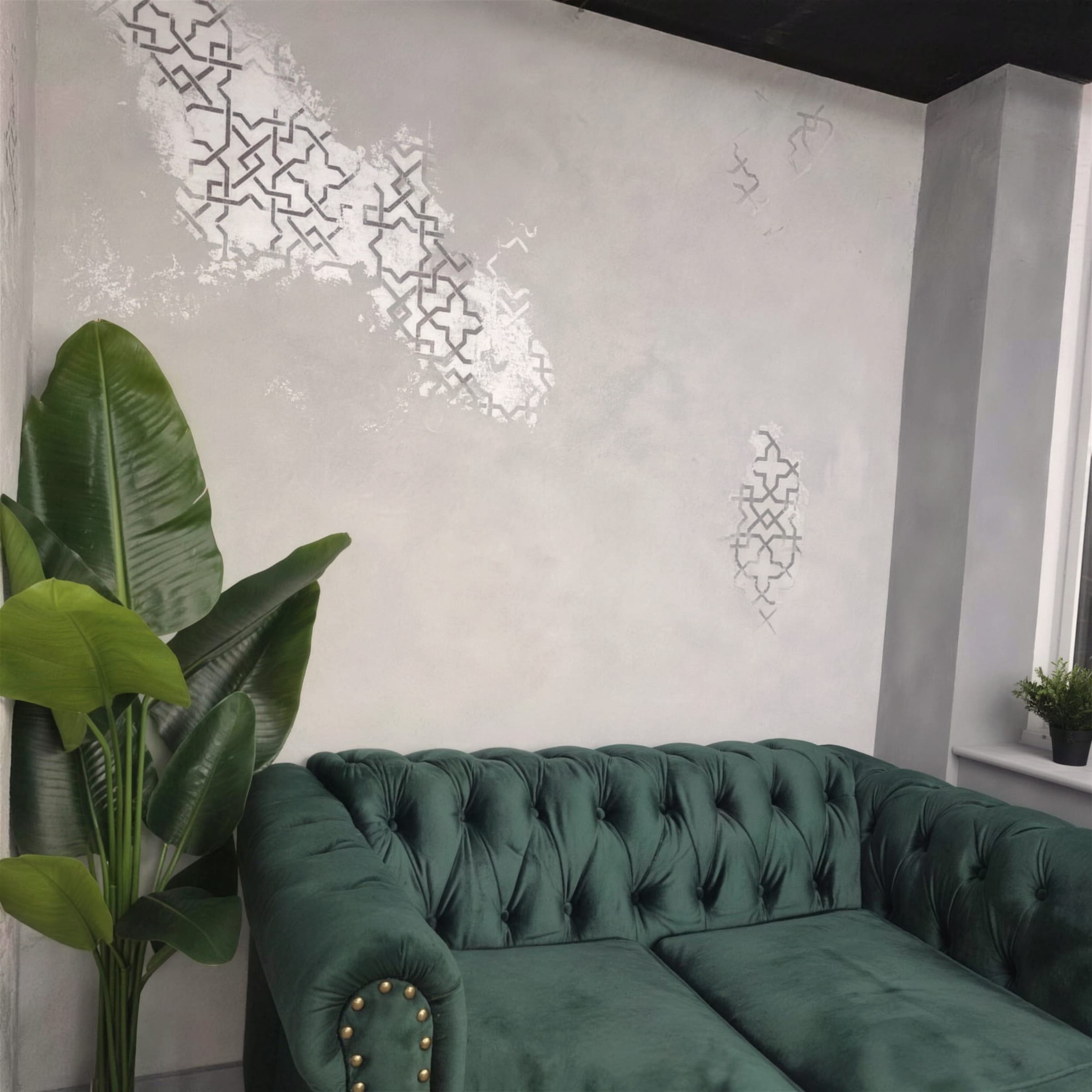 Pearl-lustre plaster wall with silver geometric stencil work behind an emerald green Chesterfield sofa and potted palm.