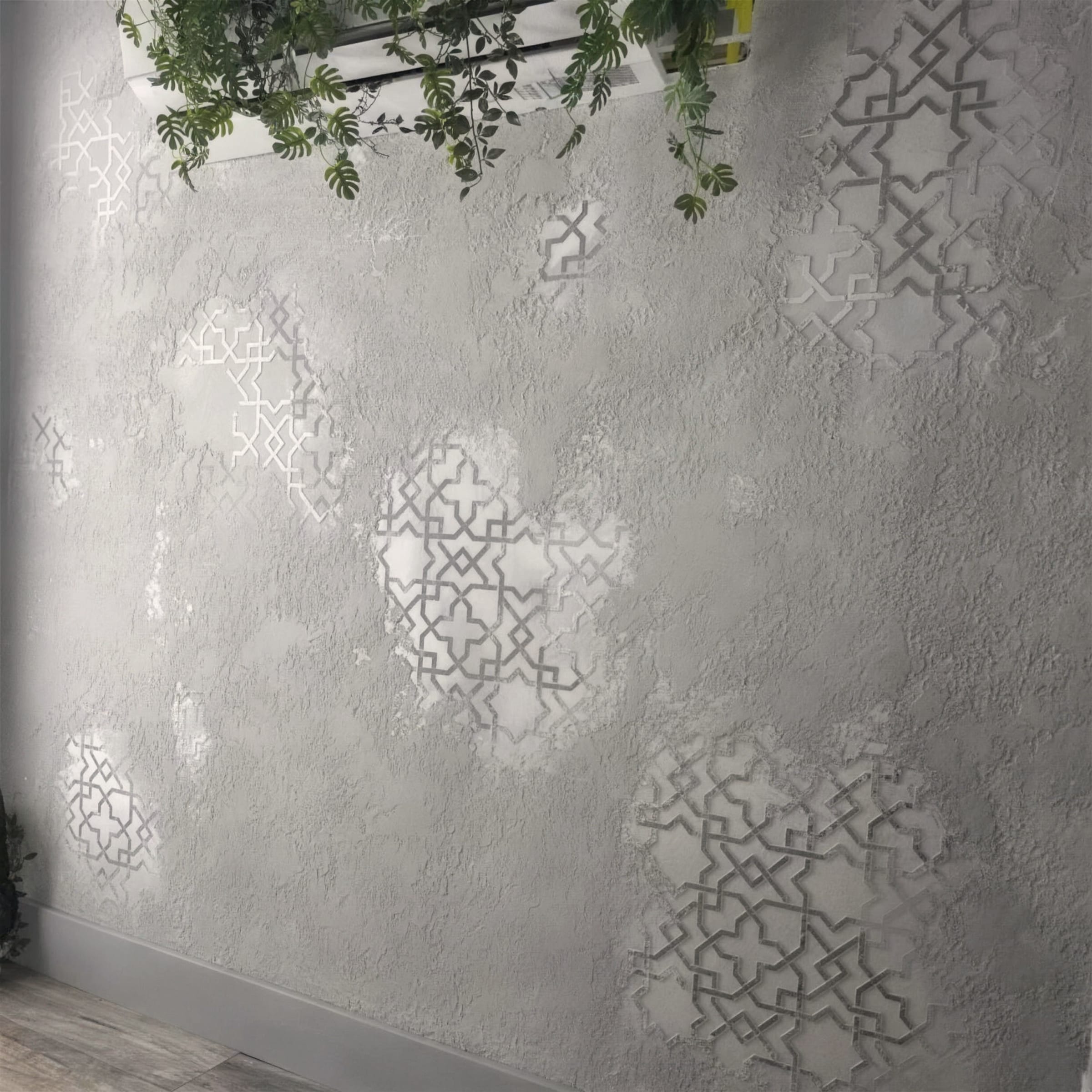 Pale grey rustic travertine plaster wall with recessed Moorish geometric stencil motifs, softened by trailing greenery along the top.