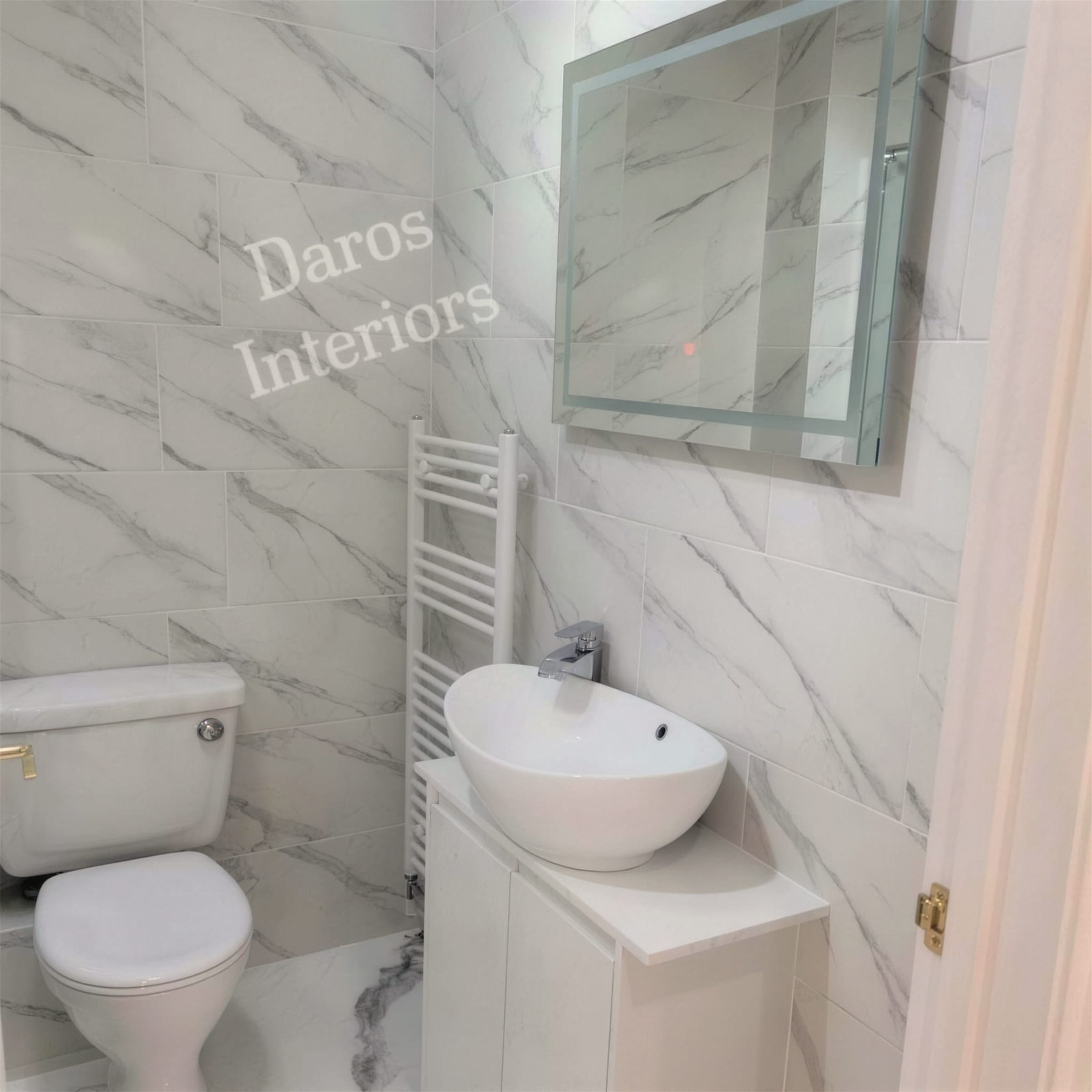 Small bathroom finished in white Calacatta-style marble-effect wall surfaces with towel radiator, countertop basin and LED mirror.