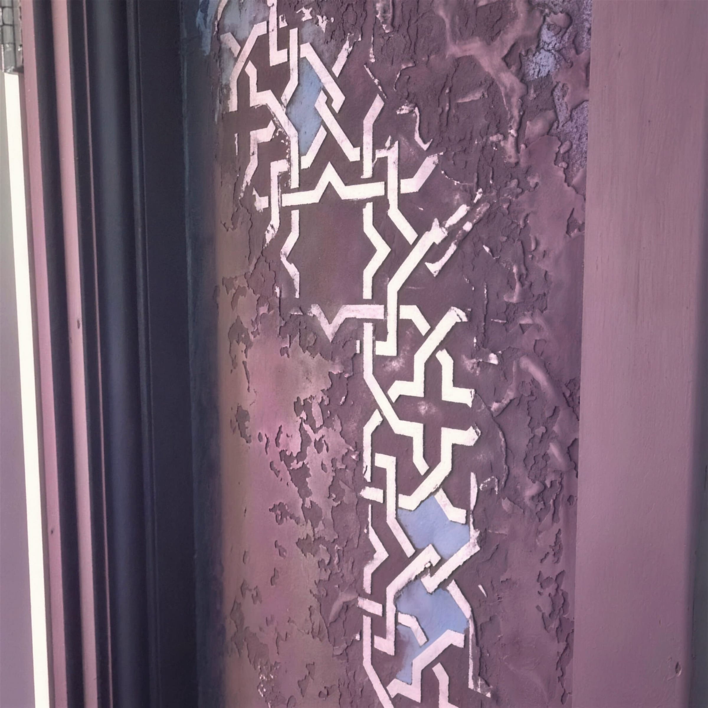 Close detail of purple-bronze distressed plaster with a silver interlocking geometric stencil band running down a reveal.