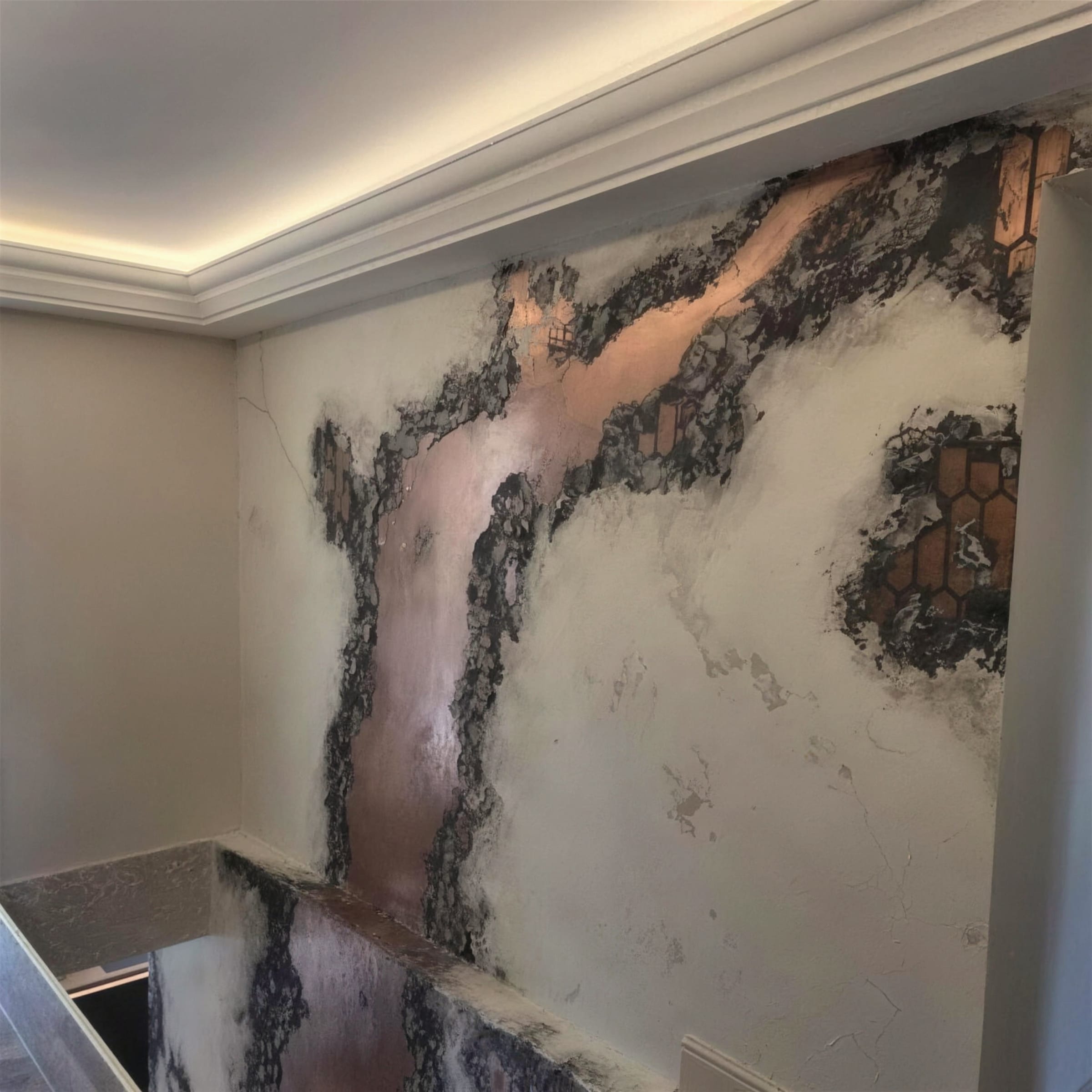 Detail of an oxidised copper metallic plaster feature wall with black patina veining, meeting a lit cornice above a stairwell.