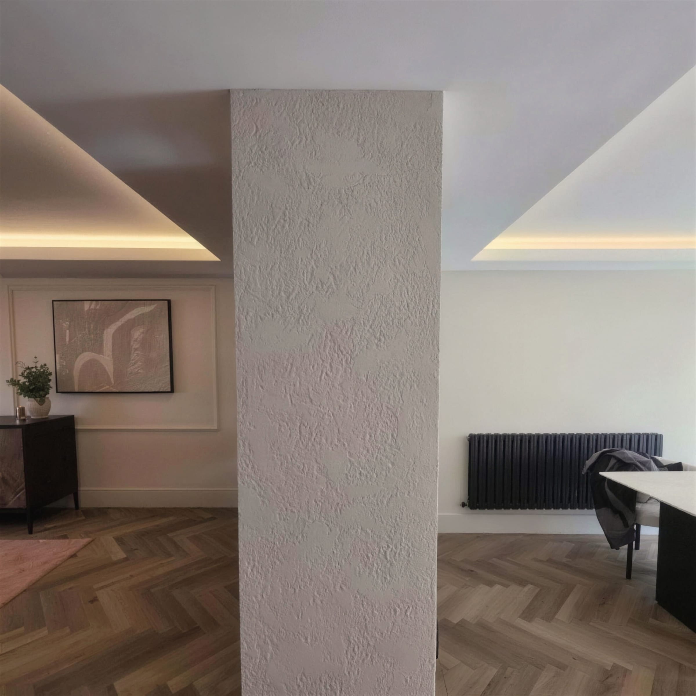 Centred textured-plaster column dividing two rooms, flanked by warm LED cove ceilings and herringbone flooring.