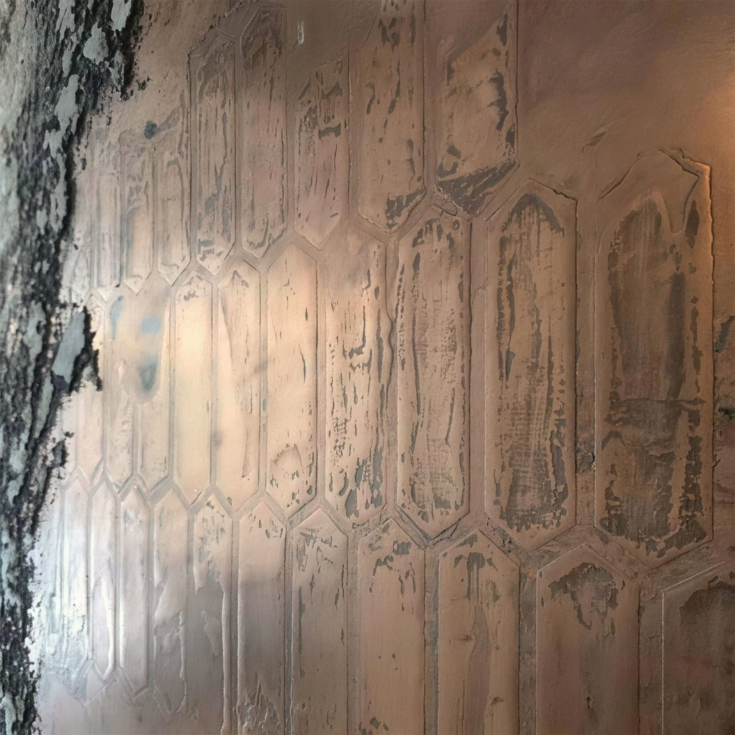 Metallic plaster wall worked into an elongated hexagon picket pattern in aged bronze and pewter tones under warm side light.