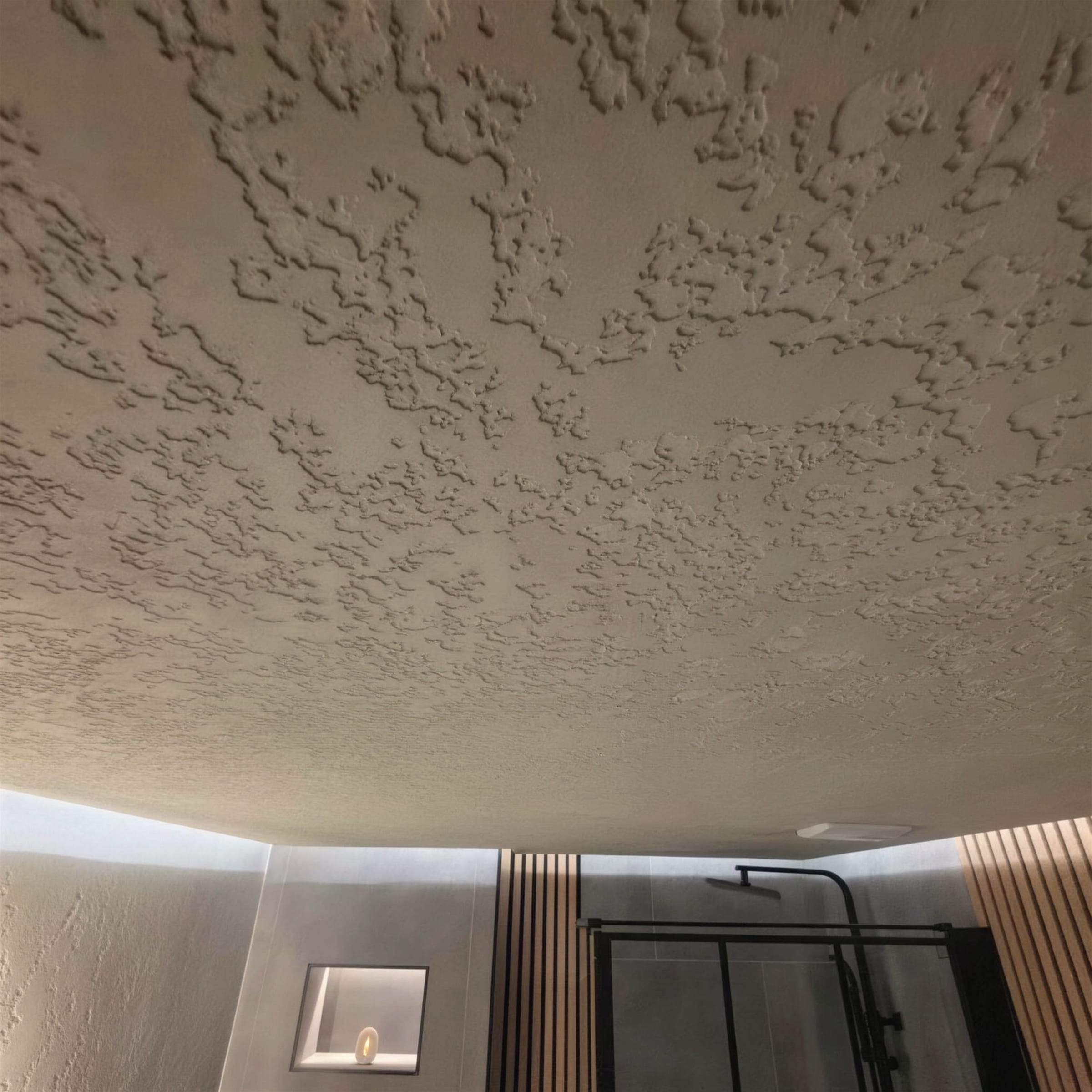 Unusual detail: pitted travertine plaster applied to a bathroom ceiling, timber slat wall and lit niche below.