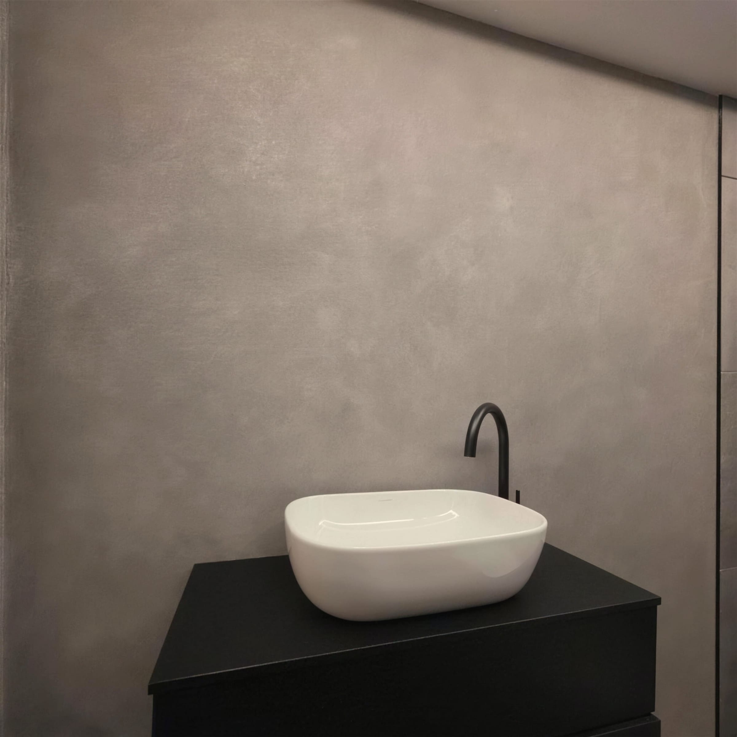 Restrained, elegant frame: soft cloudy grey marmorino wall, white oval basin and black gooseneck tap on a matte black vanity.