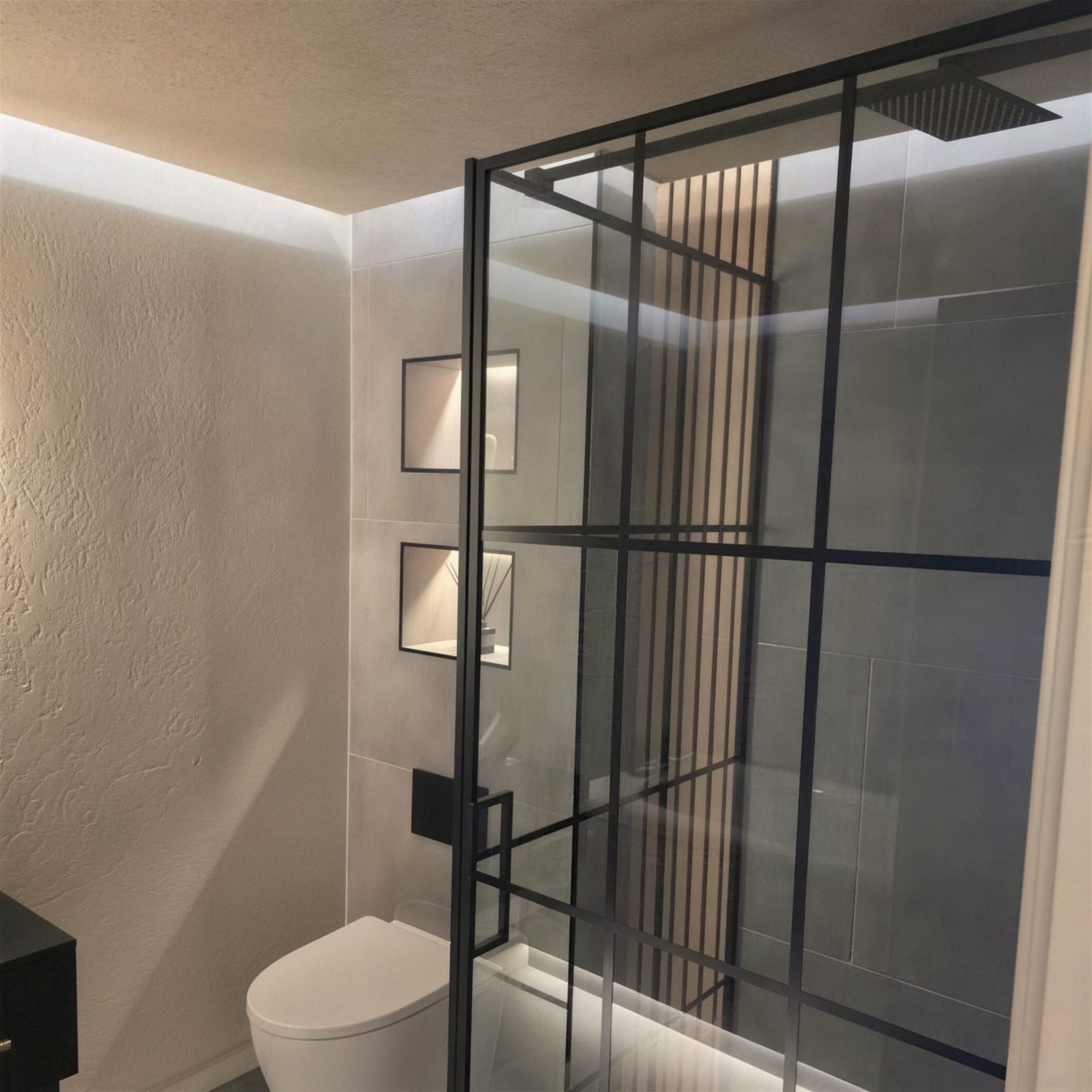 Finished bathroom: cream textured plaster on walls and ceiling, cool LED cove, Crittall-style shower screen and recessed niches.