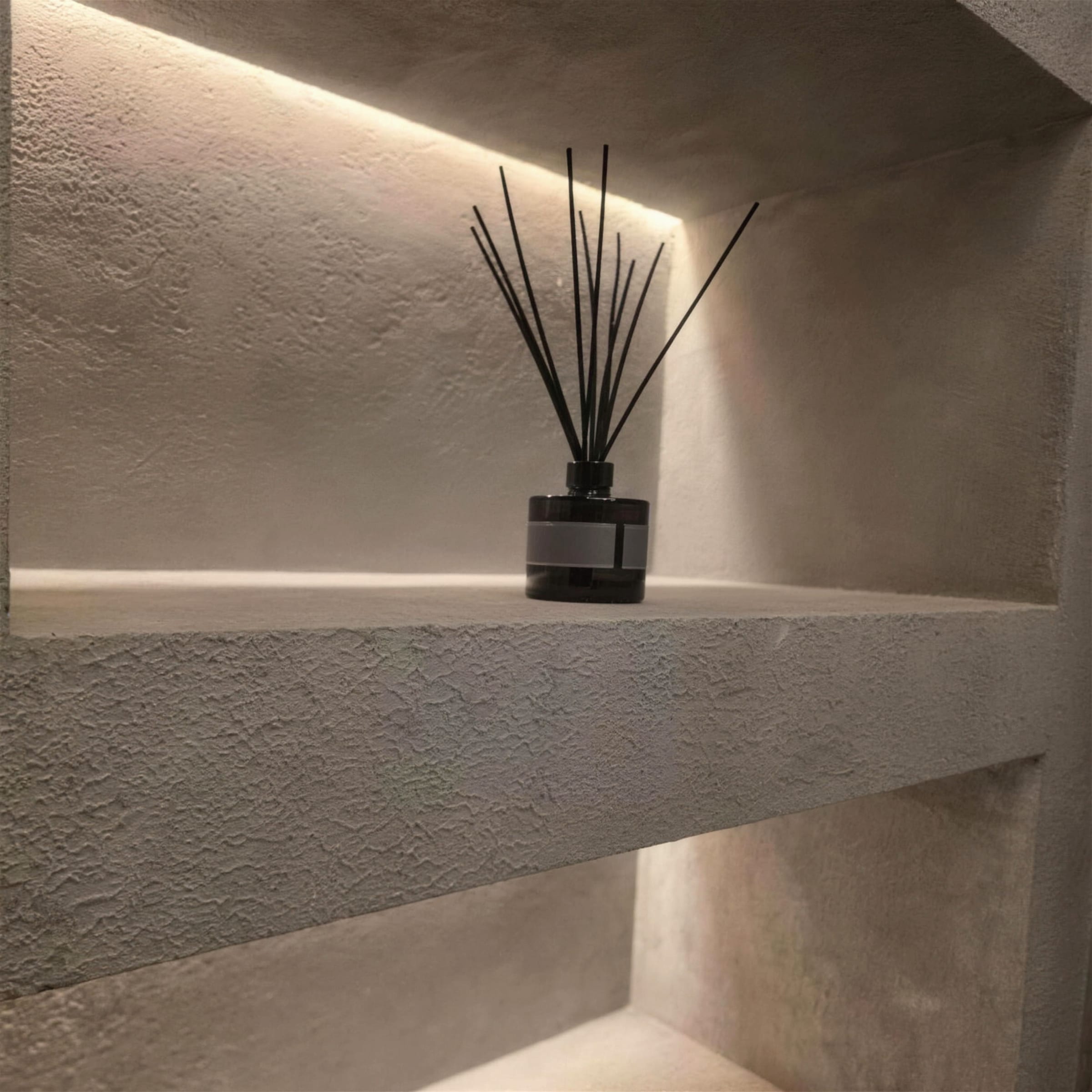 Close detail of an LED backlit display niche in heavily textured rustic travertine plaster, styled with a black reed diffuser.