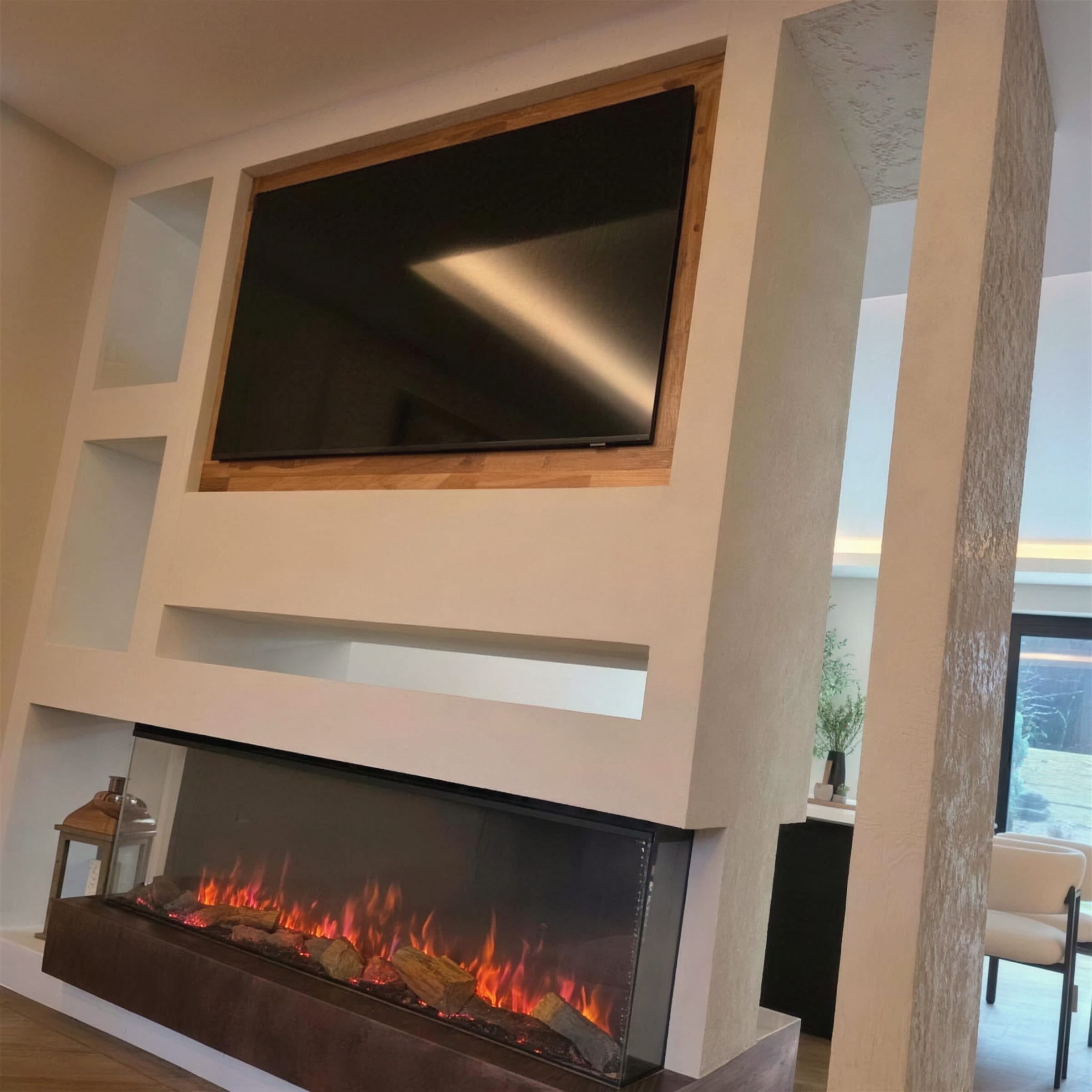 Double-sided room-divider media wall in textured white plaster with a recessed TV in a timber reveal and panoramic fireplace, lit by daylight.