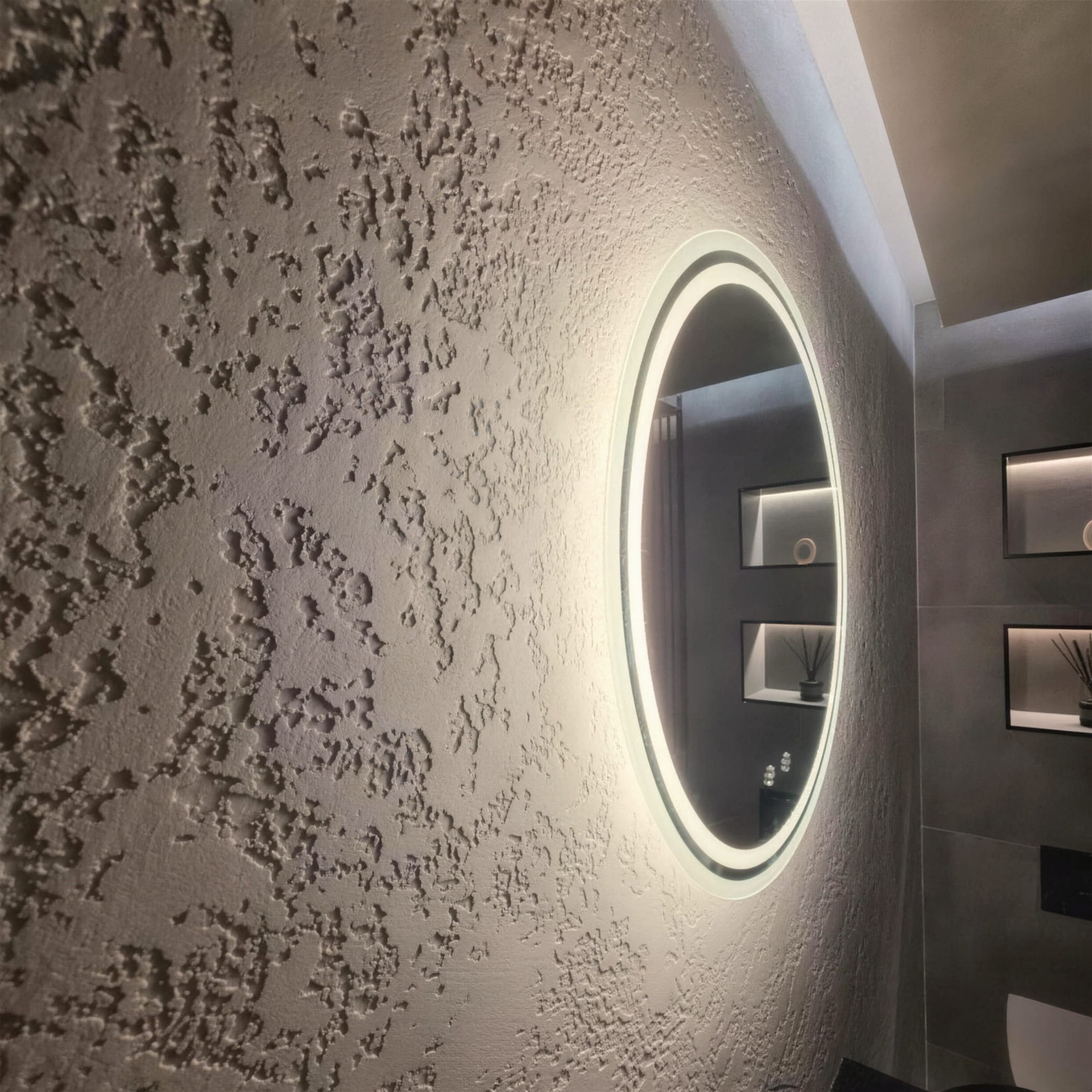 Dramatic raking light across deep rustic plaster texture, the halo mirror glowing at the edge of frame; atmospheric craft detail.