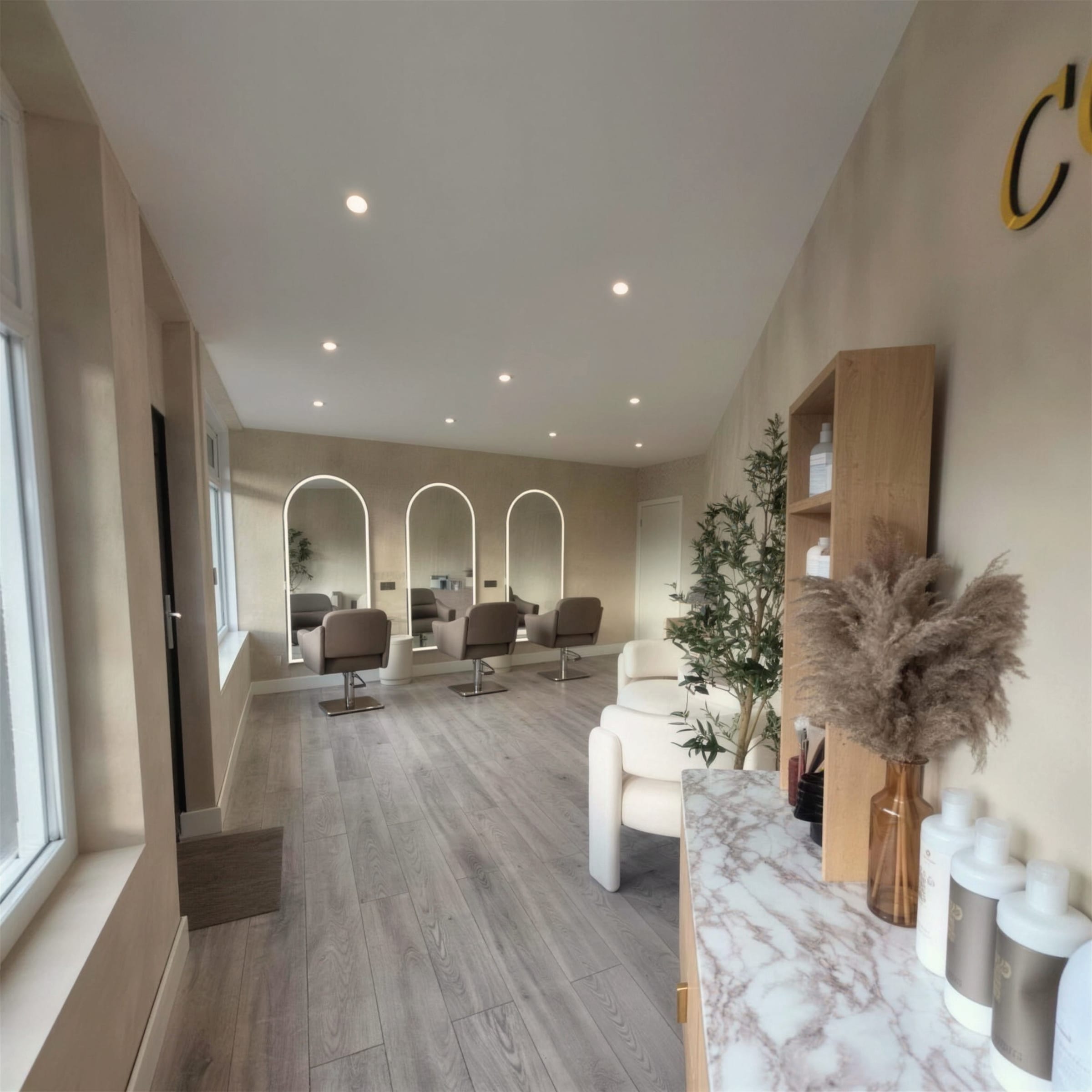 Wide view of the finished salon: limewash plaster walls, arched LED mirrors down one side, marble-topped counter styled with pampas grass.