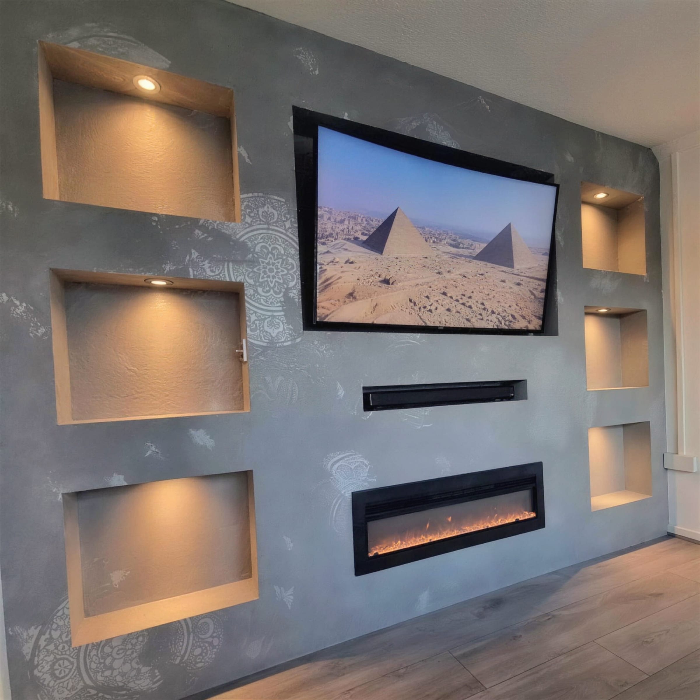 Full concrete-effect plaster media wall with raised damask stencil work, six warm-lit niches, TV and linear fireplace.