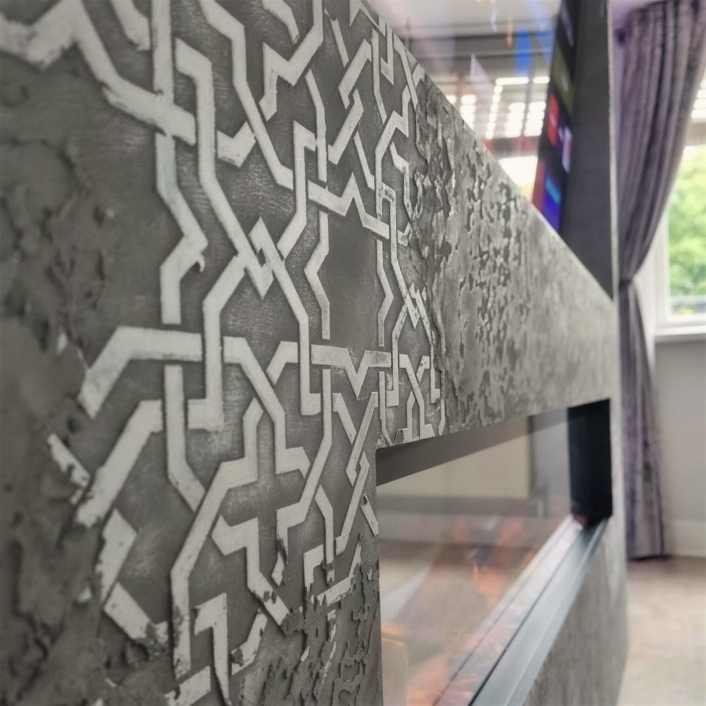 Artistic shallow-focus macro of white geometric stencil relief in grey concrete-effect plaster on a fireplace surround.