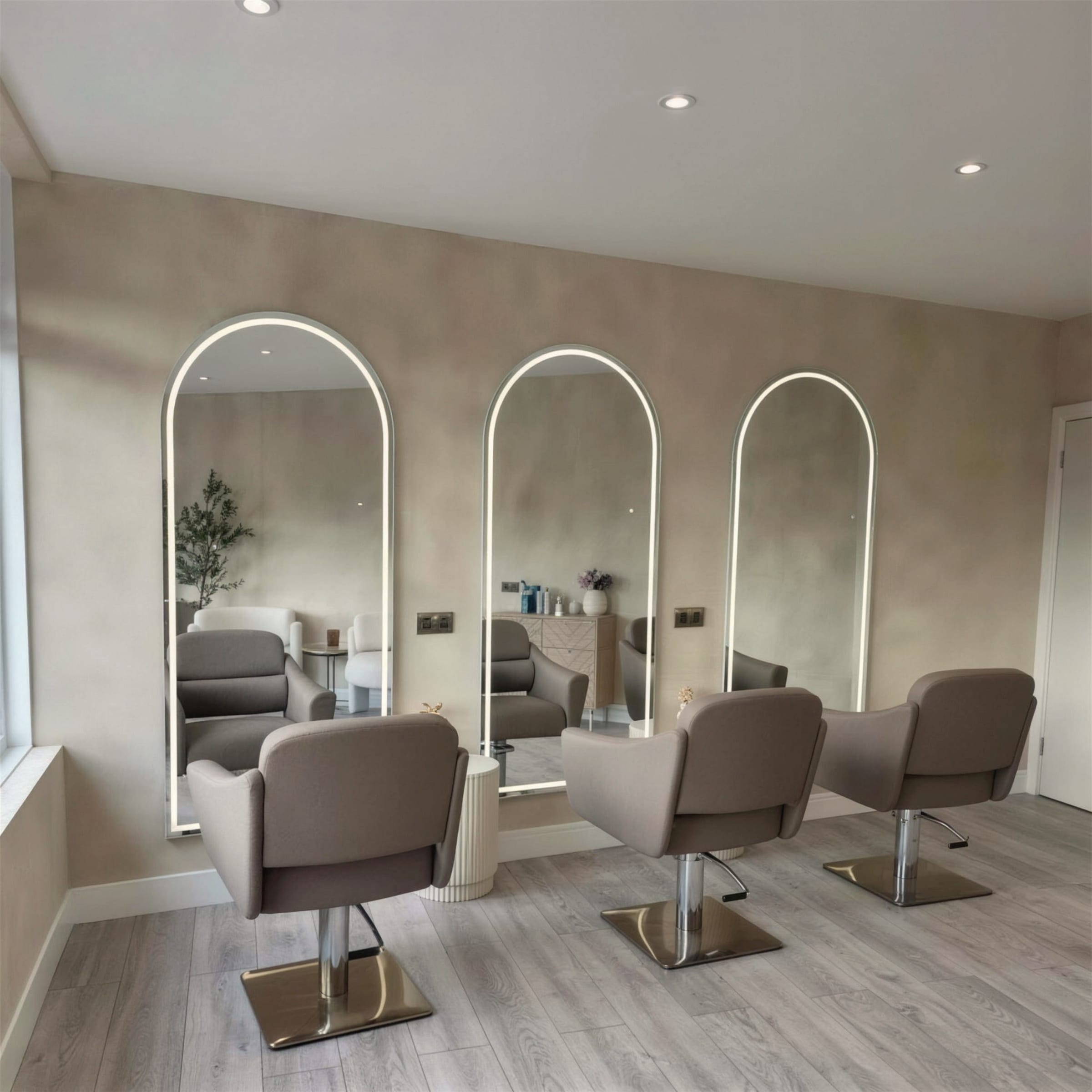 Finished salon with three LED-haloed arch mirrors set against soft clouded cream marmorino walls, taupe styling chairs and pale timber flooring.