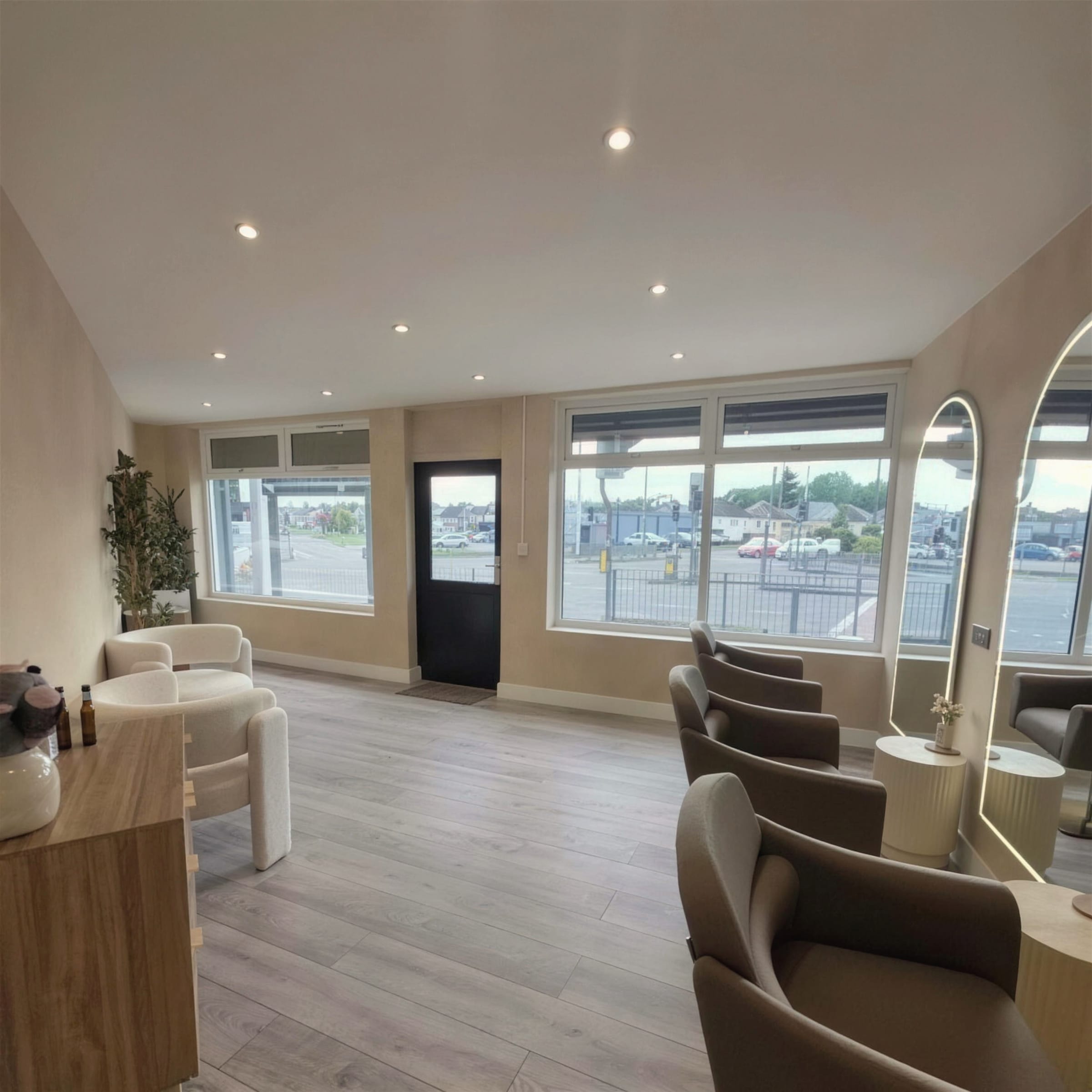 Wide view of a finished salon with soft cream clouded-plaster walls, large street-facing windows, LED-framed mirrors and taupe chairs on pale timber flooring.