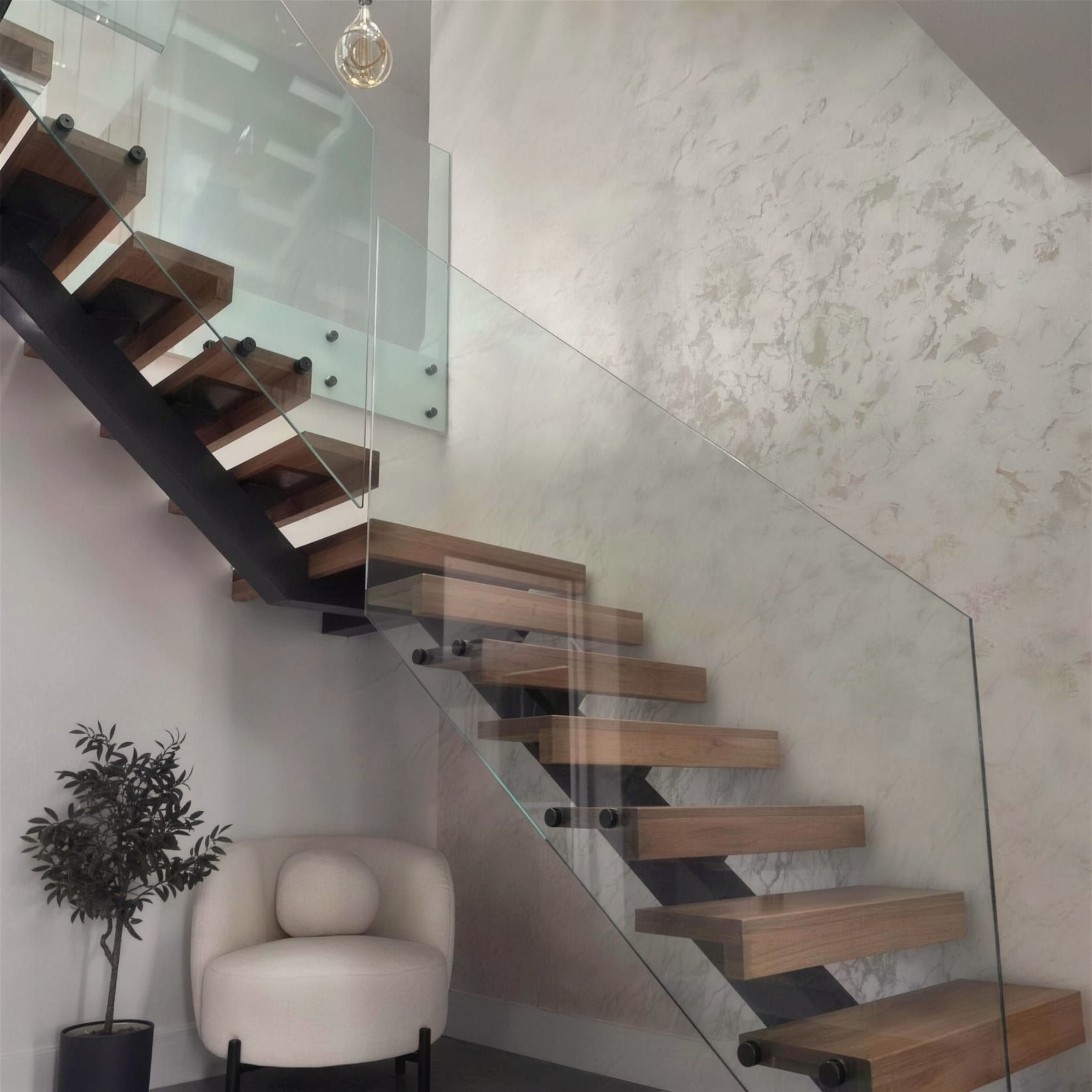Floating oak staircase with glass balustrade rising past a full-height pearlescent polished plaster feature wall, styled with a boucle armchair and olive tree.