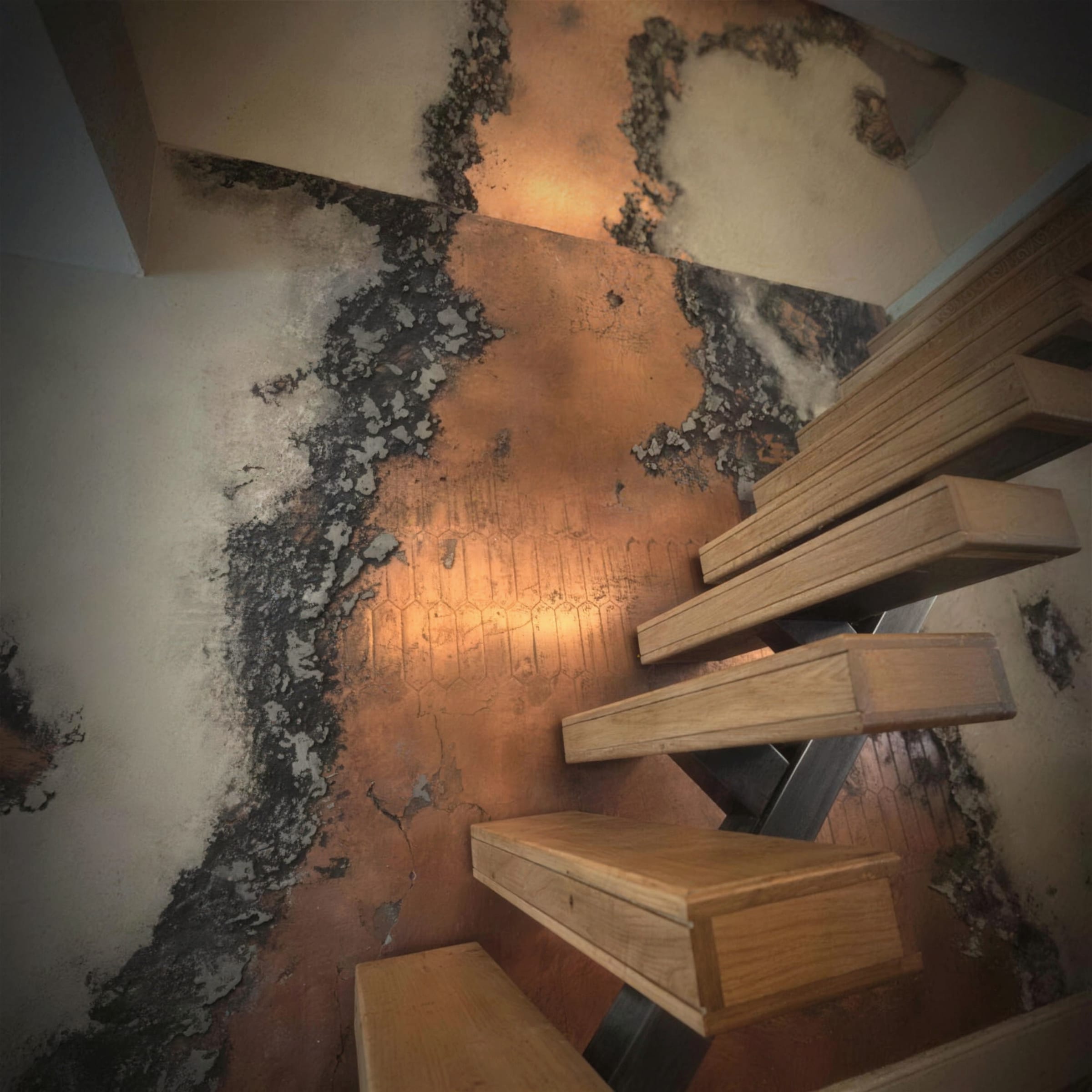 Floating oak stair treads on a black steel spine climbing past a dramatic oxidised copper and charred-texture plaster feature wall, shot on a striking diagonal.