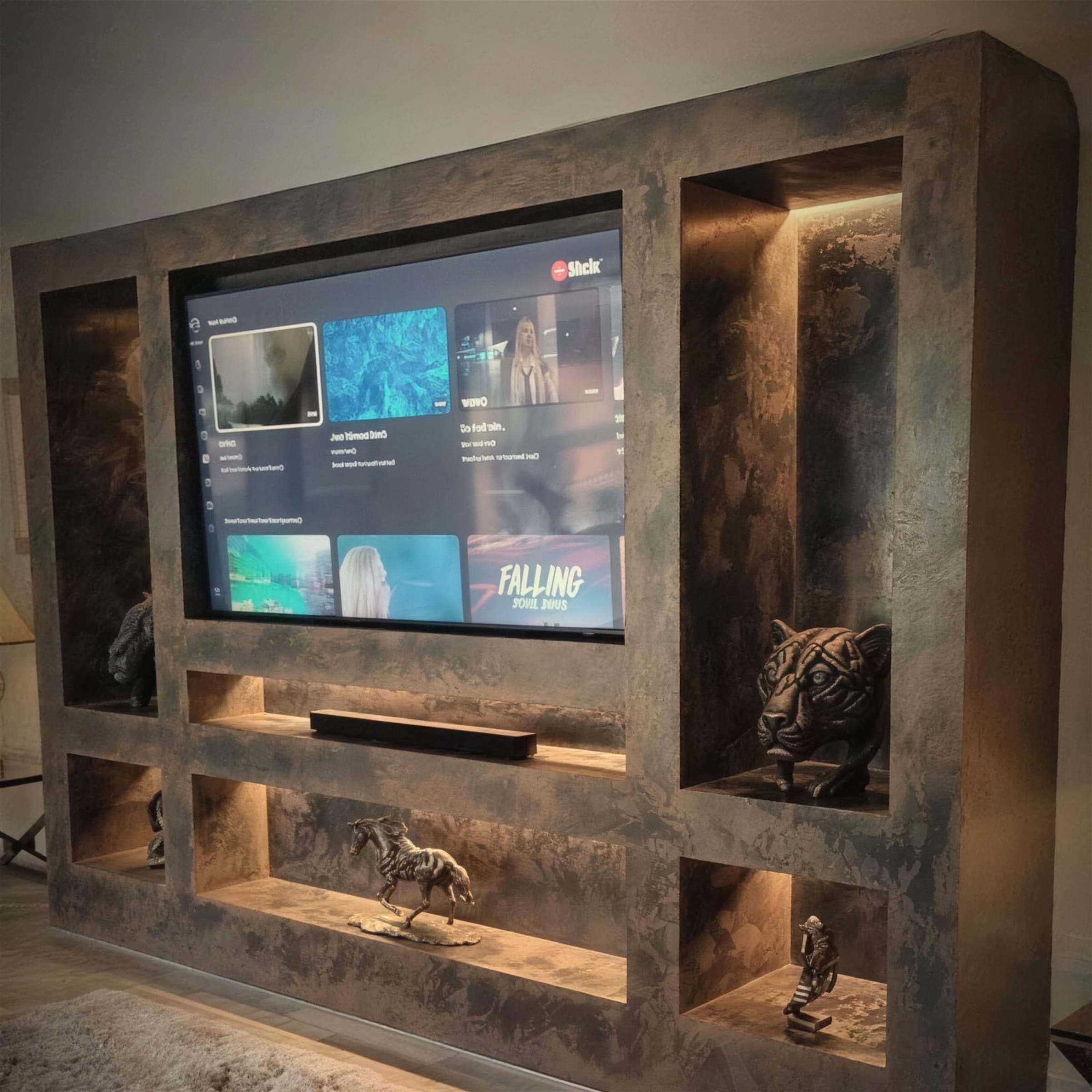 Bespoke media wall finished in dark oxidised rust-effect metallic plaster with warm LED-lit display niches framing a wall-mounted TV.