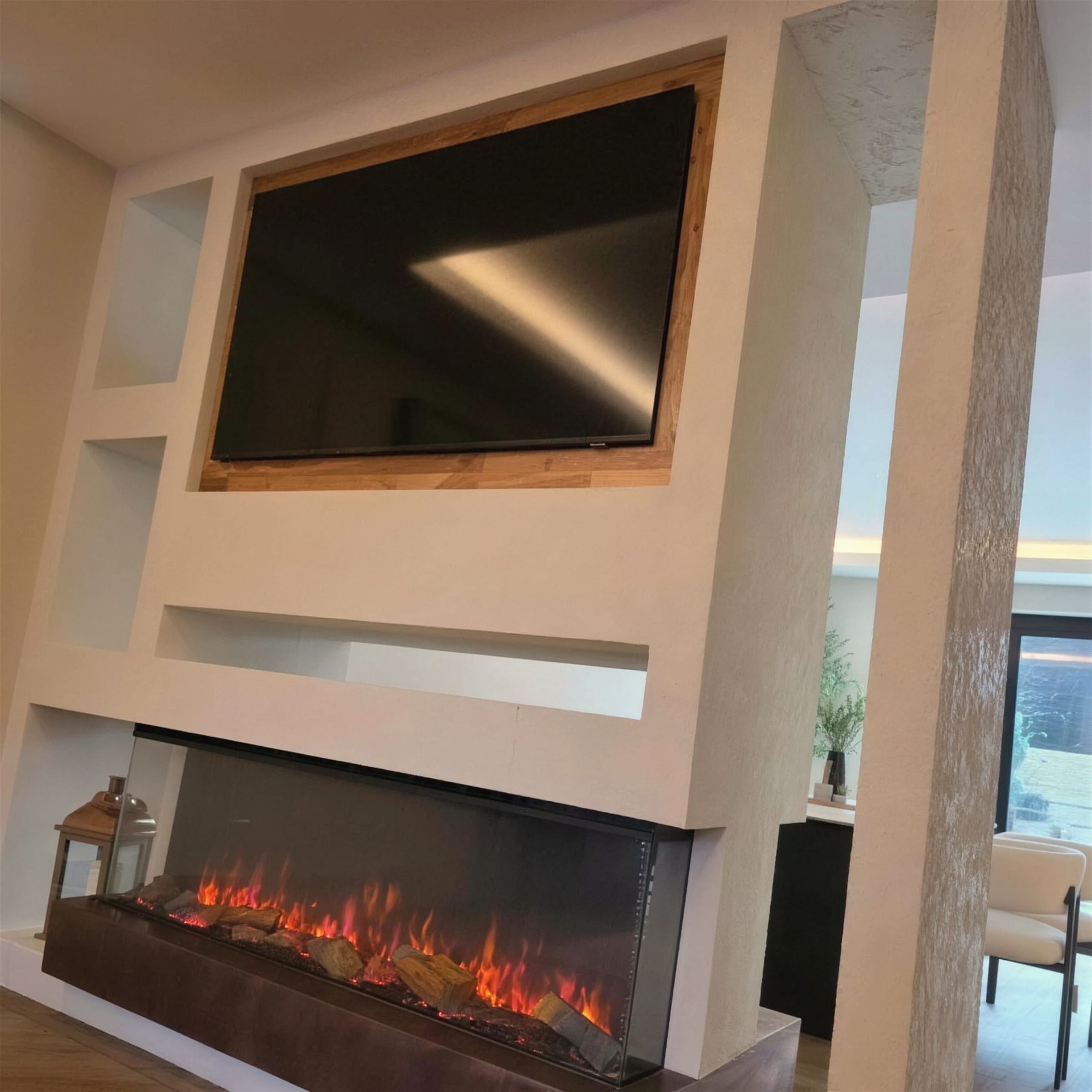 Finished white textured plaster media wall with recessed TV in a timber surround and a wide linear fireplace with flames lit below.