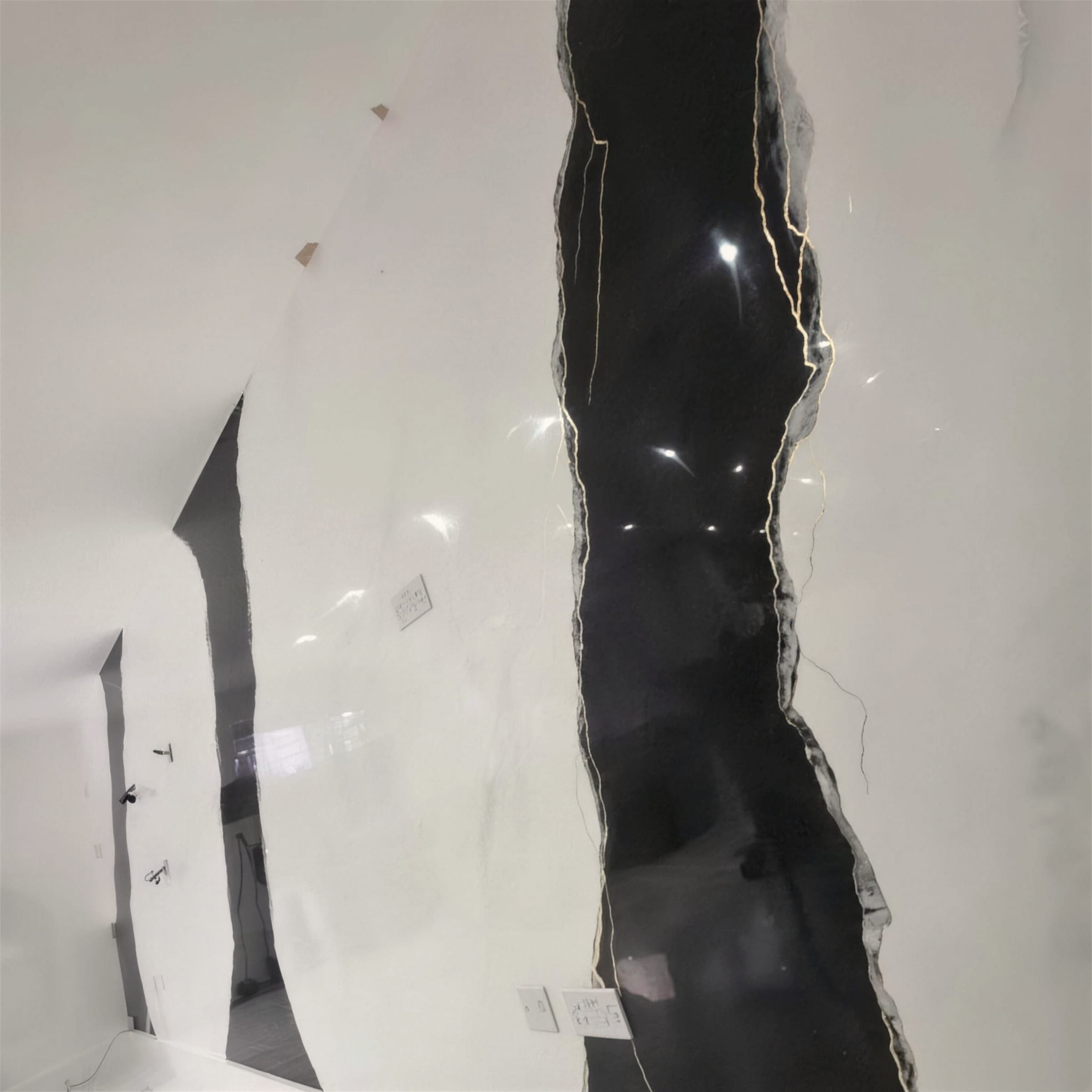 High-gloss black torn-edge feature with gold crackle borders cutting through a white polished plaster wall.